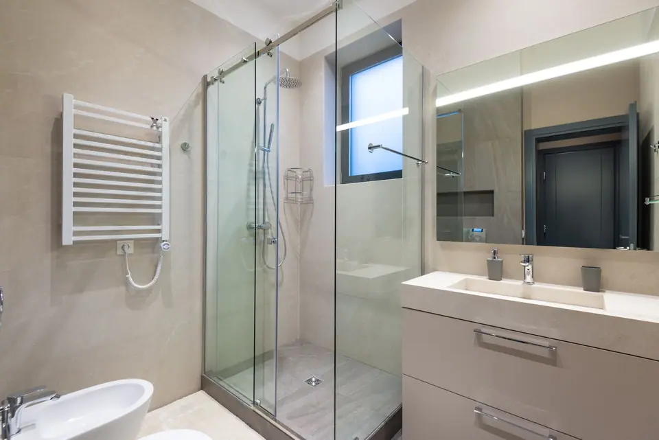 Banheiro moderno com box de vidro, espelho iluminado e gabinete suspenso